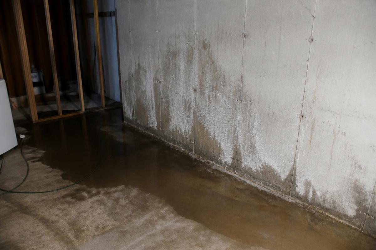 Basement floor with standing water and damp staining along the concrete wall before repair
